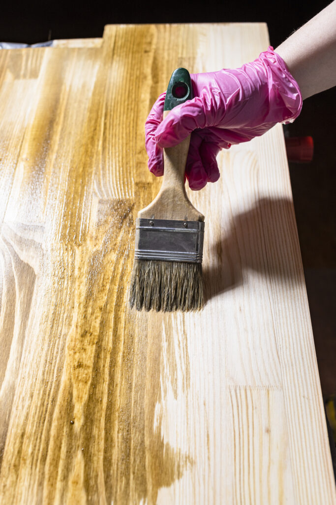 Pink gloved hand applying stain to wood