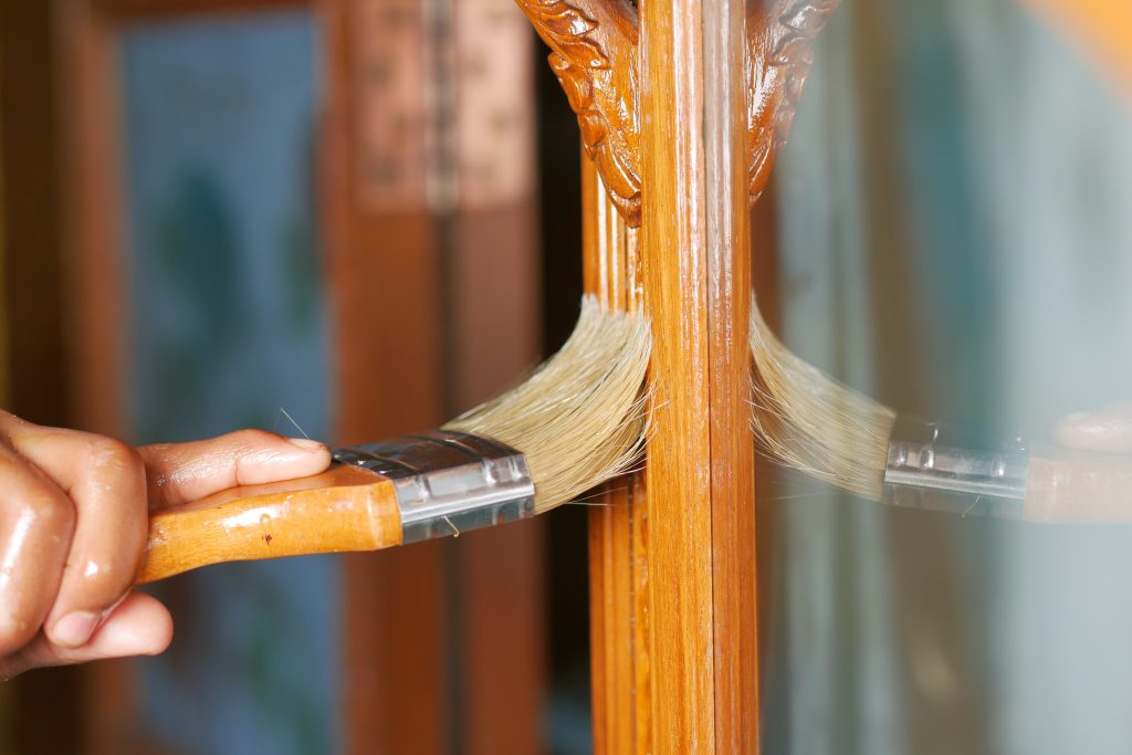 Brush applying finish to a carved wood furniture piece