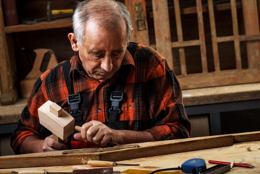 Carpenter shaping wood with a hammer and chisel at his bench