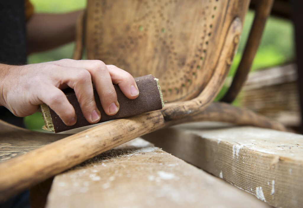 Hand sanding the worn frame of a vintage chair during restoration
