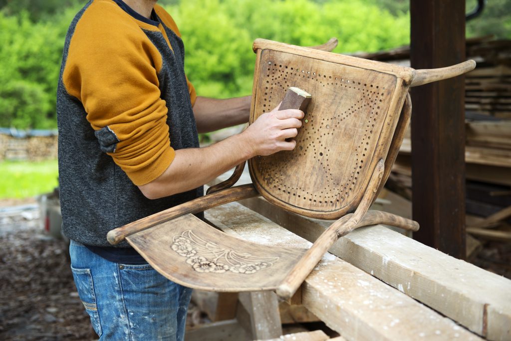 Sanding the seat of an antique cane chair outdoors