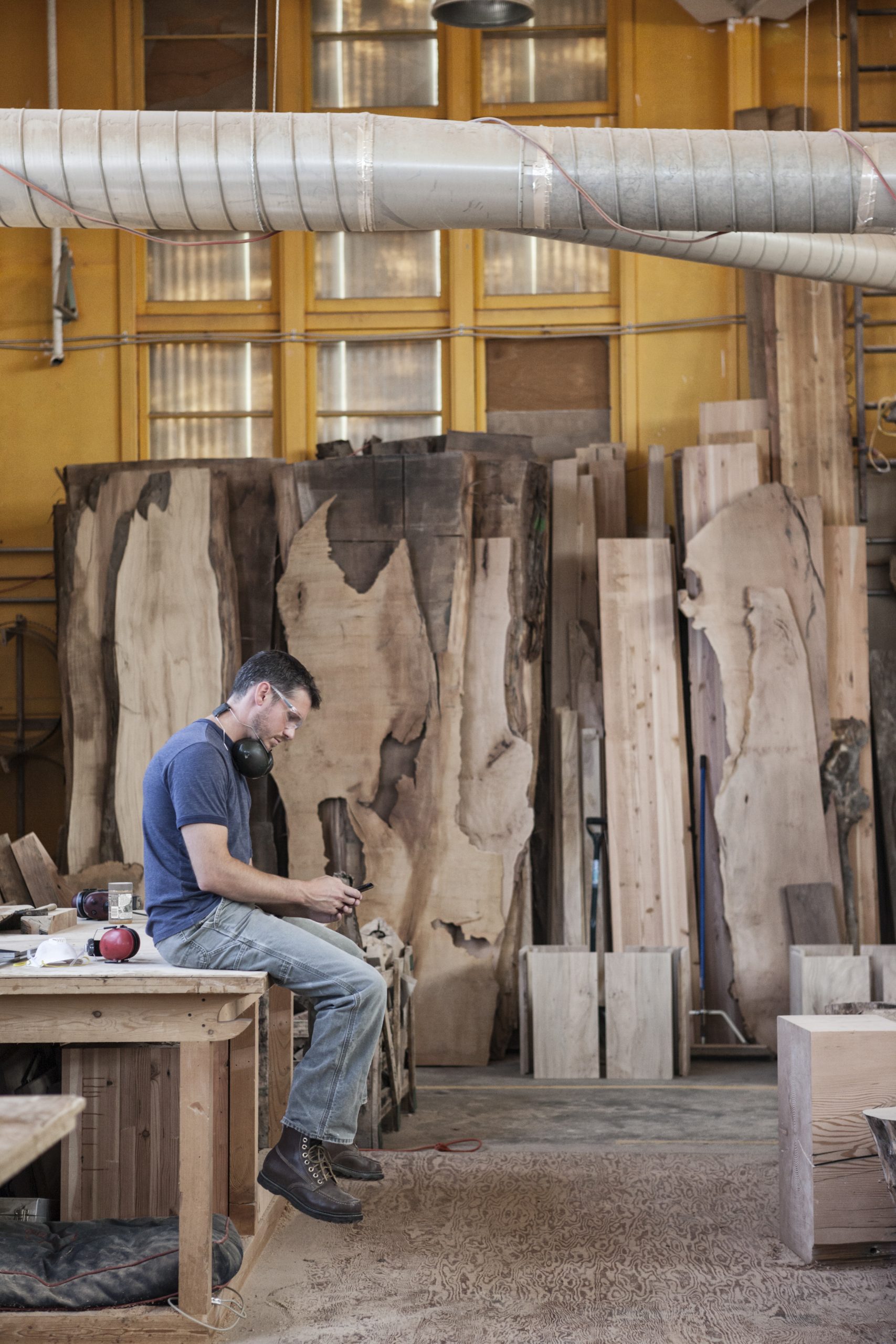 Woodworker taking a break among stacked rough-sawn lumber slabs
